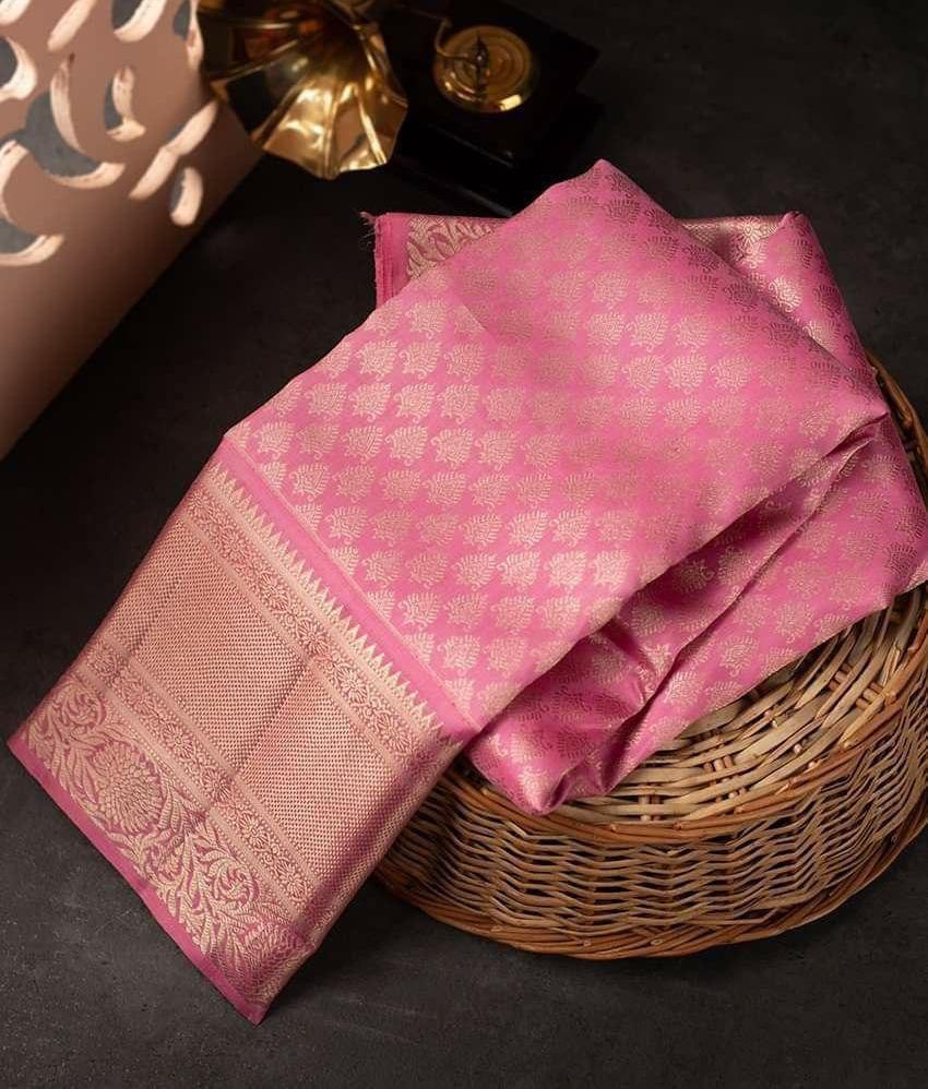 A folded pink Kanjivaram silk saree with a woven gold border, resting on a wicker basket