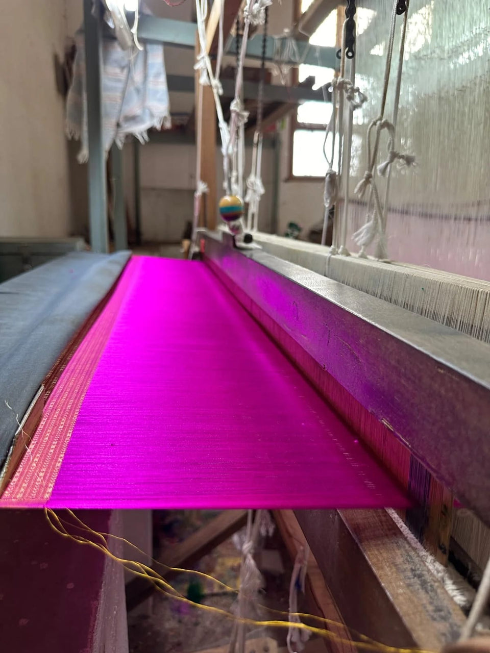 Magenta warp threads stretched across a wooden handloom in a weaving workshop