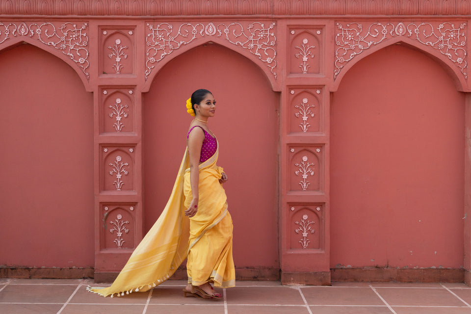 A woman in a yellow saree walking past carved terracotta arches